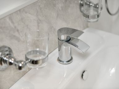 A close-up of a chrome faucet and two glass holders mounted on a tiled bathroom wall at Plas Bach in Aberffraw