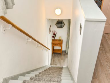 A staircase with carpet leading down to a small wooden table with a vase of flowers and a globe at Plas Bach Aberffraw
