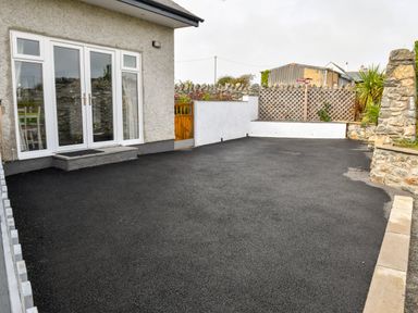 A paved driveway next to a house with glass doors and a wooden gate at Plas Bach in Aberffraw