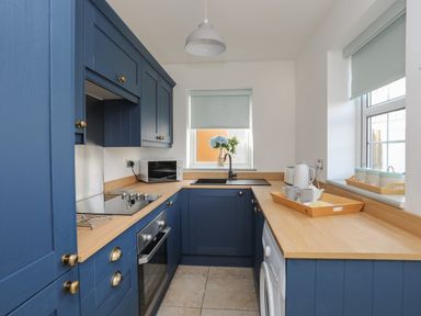 A kitchen with blue cabinets wooden countertops a sink microwave oven and two windows at Plas Bach Aberffraw