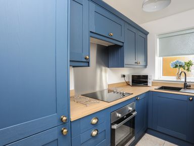 A kitchen with blue cabinets wooden countertops a black sink a microwave oven and a window with a rolled blind at Plas Bach in Aberffraw