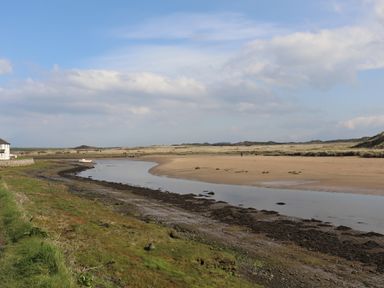 A river with grassy and sandy banks under a blue sky at Plas Bach in Aberffraw