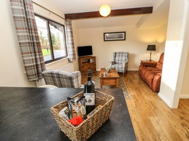 A living room with plaid armchairs a brown sofa a wooden coffee table and a basket with wine and snacks on a countertop at Snowdrop in Saltburn-by-the-Sea