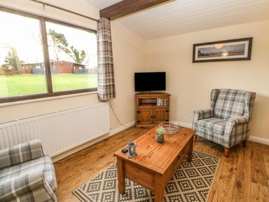 A sitting room with two plaid armchairs a wooden coffee table a TV on a wooden stand and a large window at Snowdrop in Saltburn-by-the-Sea