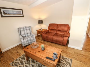 A living room with a brown sofa a gray plaid armchair wooden coffee table and a side table with lamp at Snowdrop in Saltburn-by-the-Sea