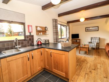 A kitchen area with wooden cabinets and black countertops next to a living room with a plaid armchair and wooden coffee table at Snowdrop in Saltburn-by-the-Sea