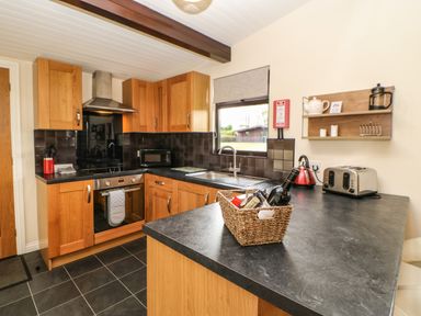 A kitchen with wooden cabinets black countertops and a basket with a wine bottle on the counter at Snowdrop in Saltburn-by-the-Sea