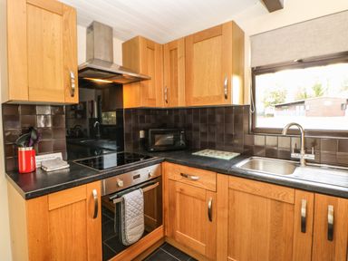 A kitchen with wooden cabinets a black countertop a stove oven microwave and a window at Snowdrop in Saltburn-by-the-Sea