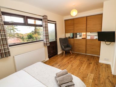 A bedroom with a bed folded towels a gray armchair wooden floor sliding closet doors and a wall-mounted TV at Snowdrop in Saltburn-by-the-Sea