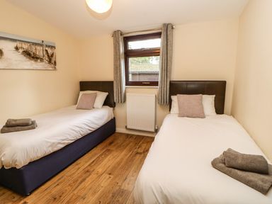 A bedroom with two single beds with pillows and folded towels on wooden floor at Snowdrop in Saltburn-by-the-Sea