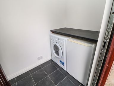 A laundry room with a washing machine and a refrigerator under a black countertop at Snowdrop in Saltburn-by-the-Sea