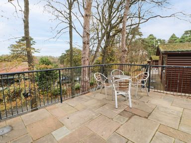 An outdoor patio with a metal table and four chairs surrounded by trees and wooden cabins at Snowdrop in Saltburn-by-the-Sea