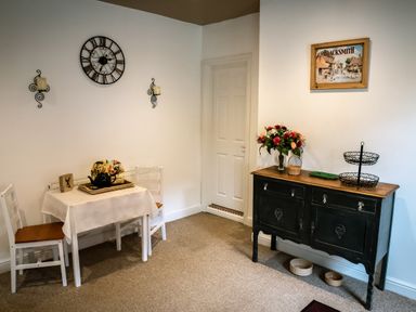 A corner dining area with a small table and two chairs a sideboard with flowers and wall clock at Anvil Lodge in Goulceby near Louth
