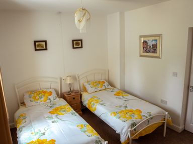 A bedroom with two single beds with yellow floral bedding a wooden nightstand and framed paintings on the walls at Anvil Lodge in Goulceby near Louth