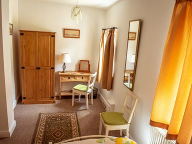 A bedroom with a wooden wardrobe a desk with a lamp and mirror two chairs with green cushions a wall mirror and yellow curtains at Anvil Lodge in Goulceby near Louth