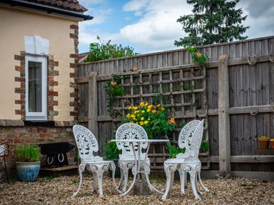 A garden patio with white metal chairs around a table and a flower arrangement against a wooden fence at Anvil Lodge in Goulceby near Louth