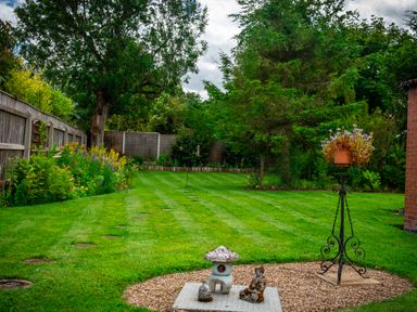 A backyard garden with striped grass and stone statues near a metal planter at Anvil Lodge in Goulceby near Louth