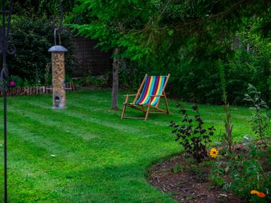 A garden with a striped deck chair a bird feeder hanging and flower beds at Anvil Lodge in Goulceby near Louth