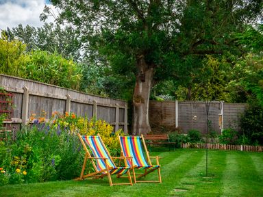 A garden with two striped deck chairs flowers and a wooden fence at Anvil Lodge in Goulceby near Louth