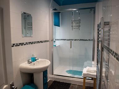 A bathroom with a pedestal sink a glass-enclosed shower a small stool with towels and a towel radiator at Anvil Lodge in Goulceby near Louth