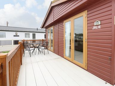 An outdoor patio with a table and four chairs next to a brown wooden building with double glass doors at Jolie in Hunstanton