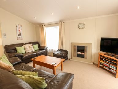 A living room with brown leather sofas a wooden coffee table a television on a stand and a fireplace at Jolie in Hunstanton