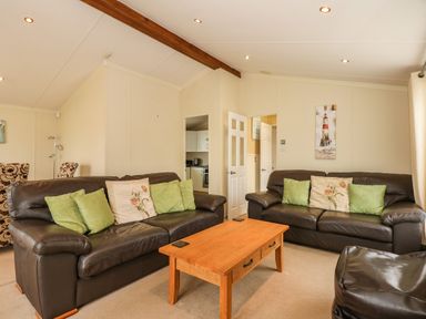 A living room with two leather sofas a wooden coffee table and cushions at Jolie in Hunstanton