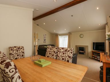 A dining area with patterned chairs and wooden table connected to a living room with sofas fireplace and television at Jolie in Hunstanton