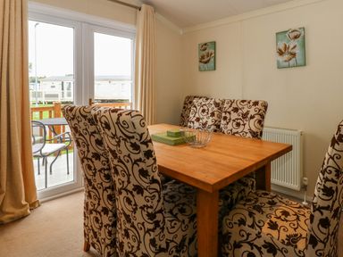 A dining area with a wooden table and six patterned upholstered chairs near sliding glass doors leading to an outdoor patio at Jolie in Hunstanton