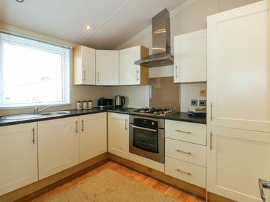 A kitchen with white cabinets a gas stove an oven a sink and a window at Jolie in Hunstanton