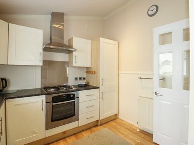 A kitchen with white cabinets black countertop stainless steel oven and stove white door with glass panels at Jolie in Hunstanton