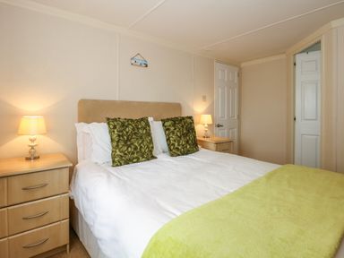 A bedroom with a double bed with green pillows and a green blanket two bedside tables with lamps and two white doors at Jolie in Hunstanton