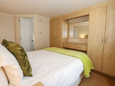 A bedroom with a bed with green pillows and blanket and built in wardrobes with a mirror at Jolie in Hunstanton