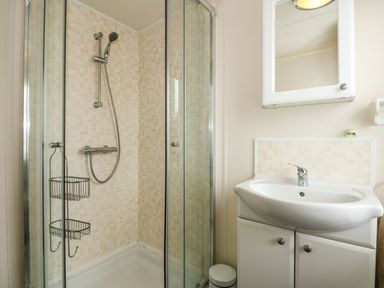 A bathroom with a glass shower enclosure and a white sink with cabinet and mirror at Jolie in Hunstanton