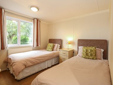 A bedroom with two single beds a nightstand and a window with curtains at Jolie in Hunstanton