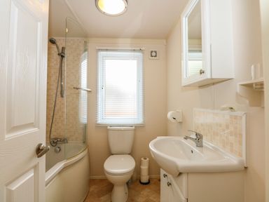 A bathroom with a bathtub and shower, toilet, sink, mirror cabinet and window at Jolie in Hunstanton