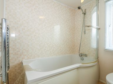 A bathroom with a bathtub shower combination and a window with blinds at Jolie in Hunstanton