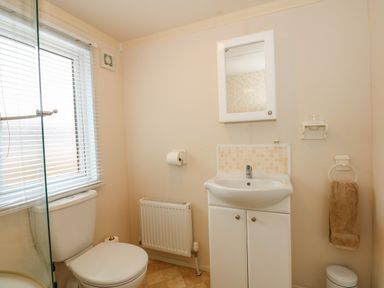 A bathroom with a toilet next to a window a sink with a cabinet and mirror a radiator and a towel hanging at Jolie in Hunstanton