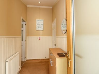 A narrow hallway with beige walls a white radiator a wooden cabinet a round wall mirror and a framed sign at Jolie in Hunstanton