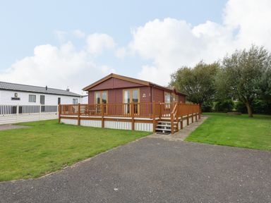 An exterior view of a single-story wooden house with a deck railing and steps on a grassy plot at Jolie in Hunstanton