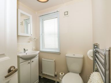A bathroom with a sink cabinet a toilet a radiator and a window with blinds at Jolie in Hunstanton