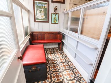 A small seating area with a wooden bench and a chest with red cushions and framed posters on the wall at The Merchant's Store in Kilrush Country Clare