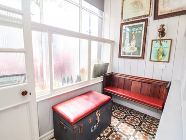 A small seating area with a wooden bench and a chest with red cushions and framed pictures on walls at The Merchant's Store in Kilrush Country Clare