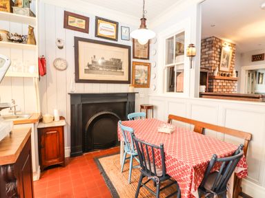 A dining area with a red patterned tablecloth on a table surrounded by blue and wooden chairs a black fireplace and framed pictures on white paneled walls at The Merchant's Store in Kilrush Country Clare
