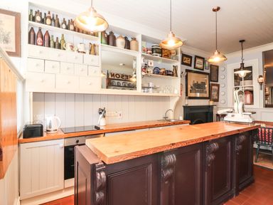 A kitchen with wooden countertops white cabinets bottles on shelves and hanging lights at The Merchant's Store in Kilrush Country Clare