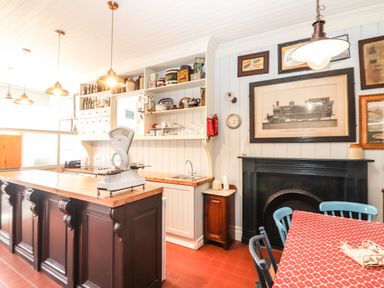 A kitchen with wooden island and scale vintage shelves with pottery red tiled floor and dining table with red patterned tablecloth at The Merchant's Store Kilrush Country Clare
