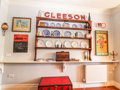A wall with shelves holding blue and white plates and various items with a wooden sign reading gleeson above at The Merchant's Store in Kilrush Country Clare