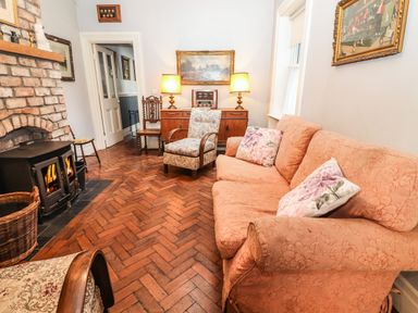 A living room with a fireplace sofa armchairs wooden floor and paintings at The Merchant's Store Kilrush Country Clare