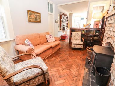 A sitting room with a peach sofa, patterned armchairs, a wood stove, a bookshelf, and a brick fireplace at The Merchant's Store in Kilrush Country Clare