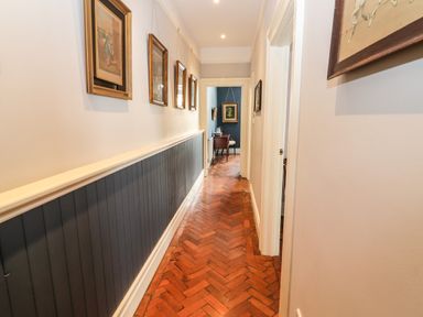 A hallway with wooden herringbone floor dark gray lower wall paneling and framed pictures at The Merchant's Store in Kilrush Country Clare